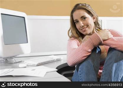 Portrait of a young woman sitting in front of a desktop PC and smiling