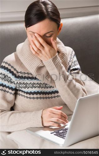 Portrait of a young woman sitting in front of her laptop on sofa and yawning
