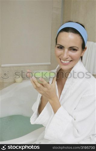 Portrait of a young woman sitting near a bathtub holding a dish of bath crystals