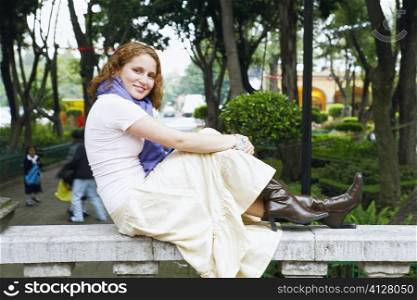 Portrait of a young woman sitting on a balustrade in a park