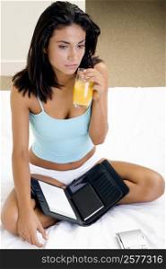 Portrait of a young woman sitting on a bed holding a glass of orange juice