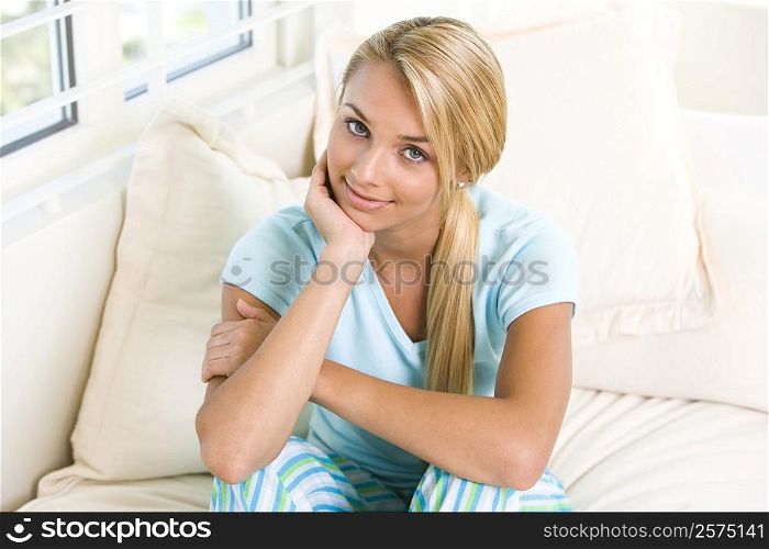 Portrait of a young woman sitting on a bed with her hand on her chin