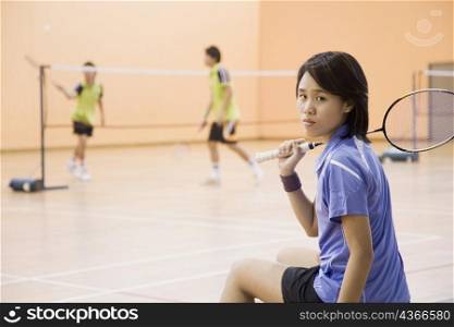 Portrait of a young woman sitting on a bench and holding a badminton racket