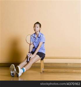 Portrait of a young woman sitting on a bench and holding a badminton racket