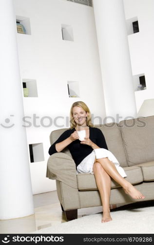 Portrait of a young woman sitting on a couch and holding a coffee cup