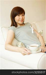 Portrait of a young woman sitting on a couch and holding a cup of tea