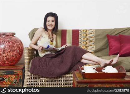 Portrait of a young woman sitting on a couch and holding a magazine