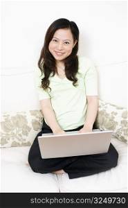 Portrait of a young woman sitting on a couch and using a laptop