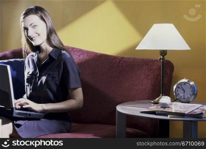 Portrait of a young woman sitting on a couch using a laptop