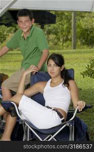 Portrait of a young woman sitting on a folding chair and holding a teenage boys hand