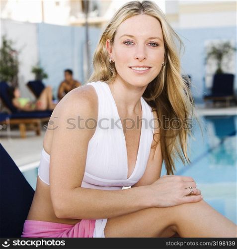 Portrait of a young woman sitting on a lounge chair at the poolside