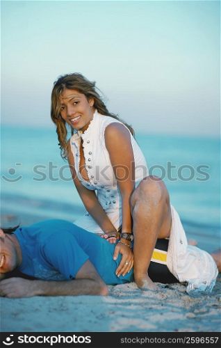 Portrait of a young woman sitting on a mid adult man&acute;s buttocks on the beach