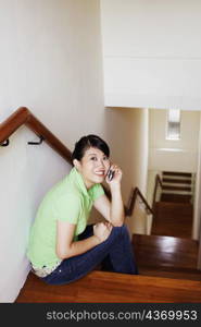 Portrait of a young woman sitting on a staircase and talking on a mobile phone