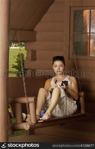 Portrait of a young woman sitting on a swing and holding a makeup brush