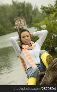 Portrait of a young woman sitting on a tree stump by the lake