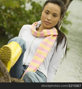 Portrait of a young woman sitting on a tree trunk by the lake