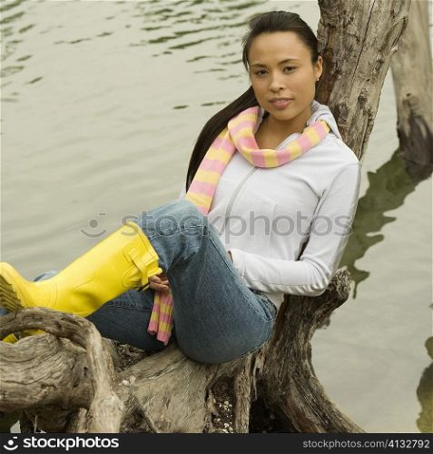 Portrait of a young woman sitting on a tree trunk by the lake