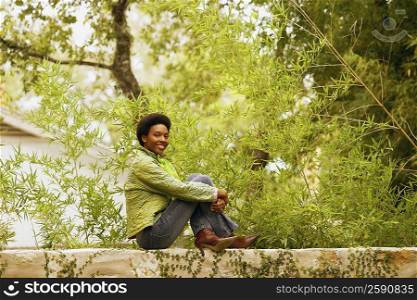 Portrait of a young woman sitting on a wall and smiling