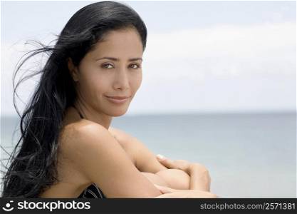 Portrait of a young woman sitting on the beach with hugging her knees