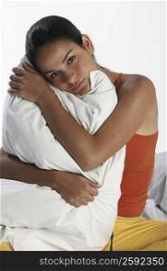 Portrait of a young woman sitting on the bed and hugging a pillow