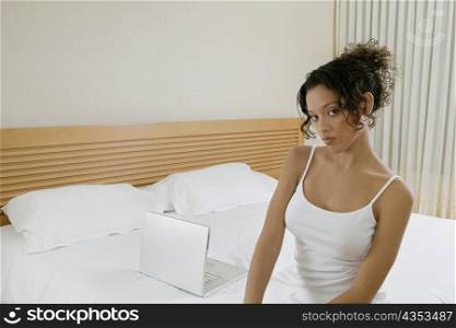 Portrait of a young woman sitting on the bed beside a laptop