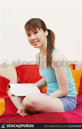 Portrait of a young woman sitting on the bed with a magazine and smiling