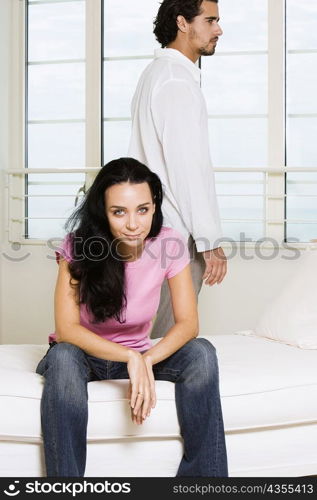 Portrait of a young woman sitting on the bed with a young man standing behind her
