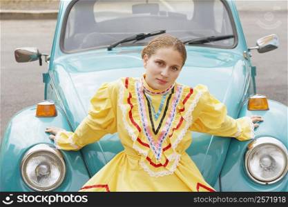 Portrait of a young woman sitting on the bumper of a car