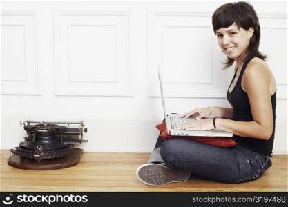 Portrait of a young woman sitting on the floor and using a laptop