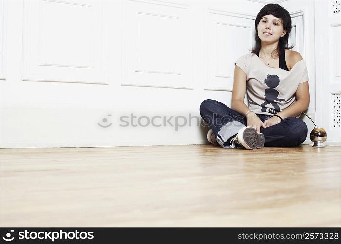Portrait of a young woman sitting on the floor at the corner of a room