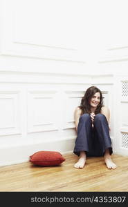 Portrait of a young woman sitting on the floor at the corner of a room