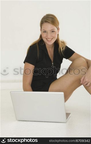 Portrait of a young woman sitting on the floor in front of a laptop