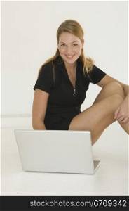 Portrait of a young woman sitting on the floor in front of a laptop