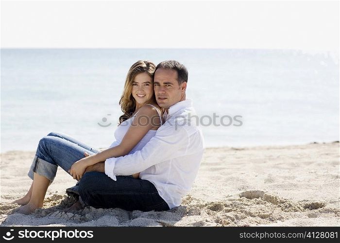 Portrait of a young woman sitting on the lap of a mid adult man on the beach