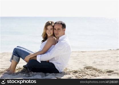 Portrait of a young woman sitting on the lap of a mid adult man on the beach