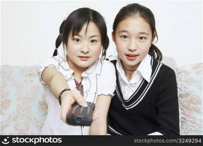Portrait of a young woman sitting together with her sister holding a remote control