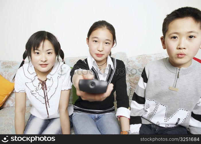 Portrait of a young woman sitting with her sister and her brother holding a remote control