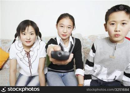 Portrait of a young woman sitting with her sister and her brother holding a remote control
