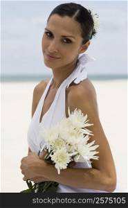 Portrait of a young woman smiling and holding flowers on the beach