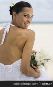 Portrait of a young woman smiling and holding flowers on the beach