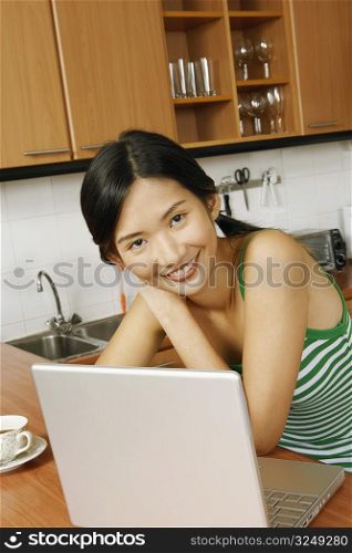 Portrait of a young woman smiling in front of a laptop at a kitchen counter