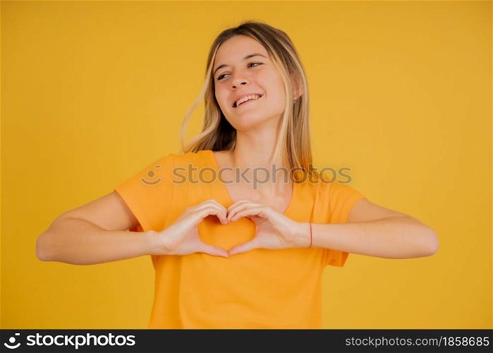 Portrait of a young woman smiling while making a heart with her hands against isolated background.
