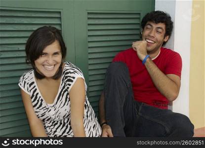 Portrait of a young woman smiling with a young man sitting beside her and coughing