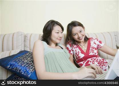 Portrait of a young woman smiling with another young woman using a laptop