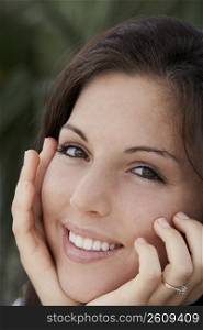Portrait of a young woman smiling with her hands on her chin