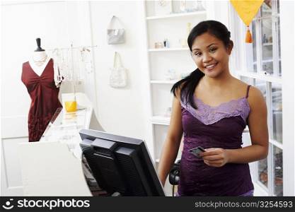 Portrait of a young woman standing at a checkout counter and holding a credit card