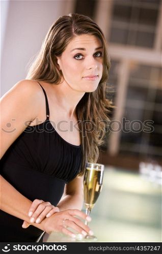 Portrait of a young woman standing at the bar counter holding a champagne flute