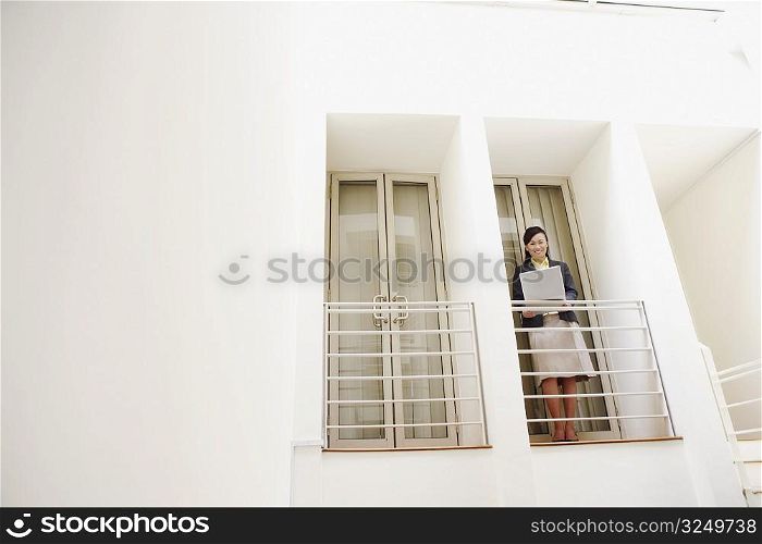 Portrait of a young woman standing at the doorway of an office and using a laptop