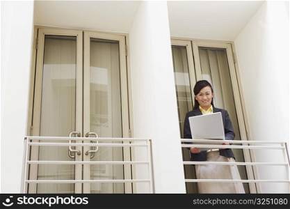 Portrait of a young woman standing at the doorway of an office and using a laptop