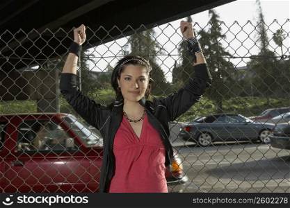 Portrait of a young woman standing in front of a chain-link fence
